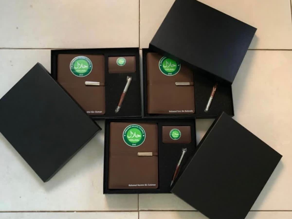 Three brown leather corporate gift sets in black presentation boxes, each with a notebook, card holder and pen branded with the Zimbabwe Halaal Council logo